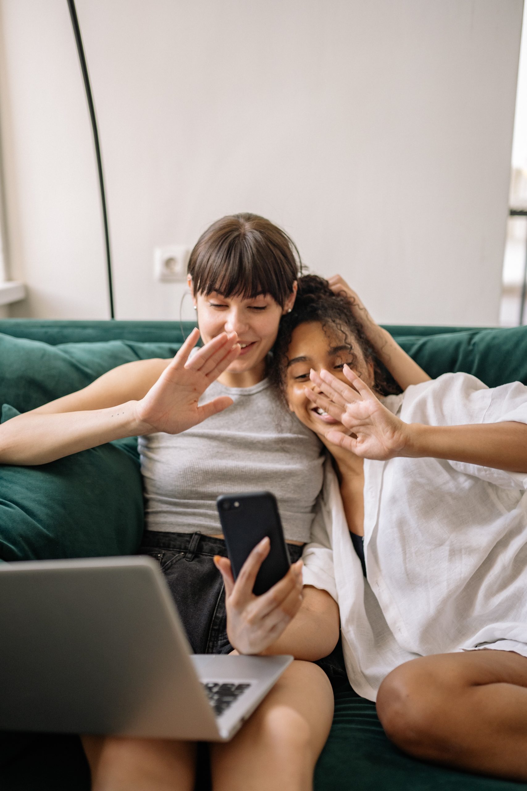 two young women smiling and waving at a smart phone