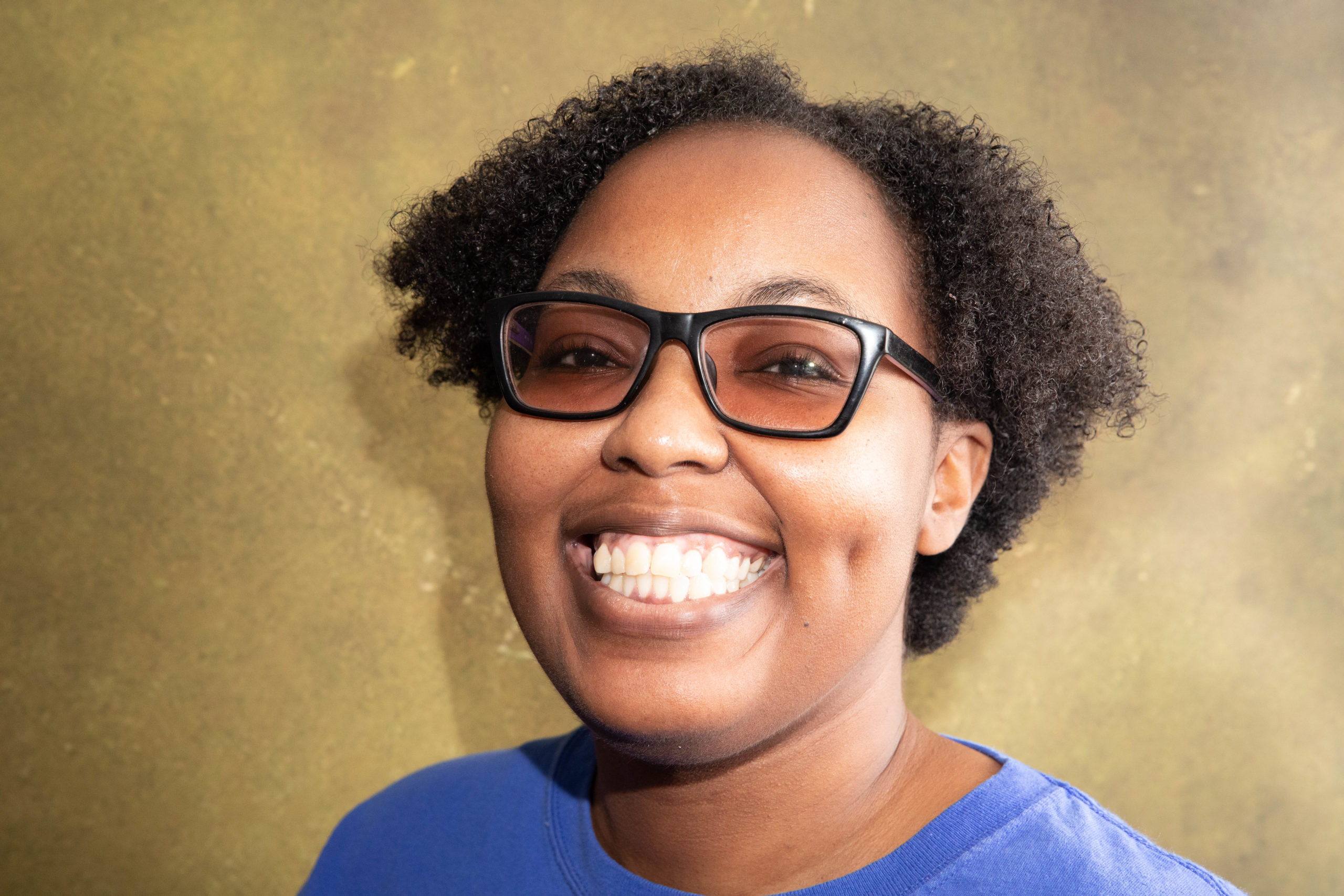 A person smiles wearing glasses and a blue shirt.
