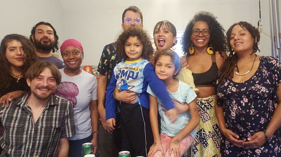 a group of people, mostly BIPOC, gathered in a room smiling at the camera.