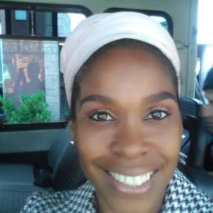 a headshot of a black woman wearing a white headwrap and checked suit